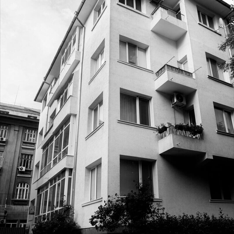 Társasházi lakóépület homlokzata, több erkélyes és nyílászárós lakással, fekete-fehér szűrővel fotózva, a közös képviselők földhivatali regisztrációjához kapcsolódó adminisztrációs folyamatok vizuális illusztrációjaként