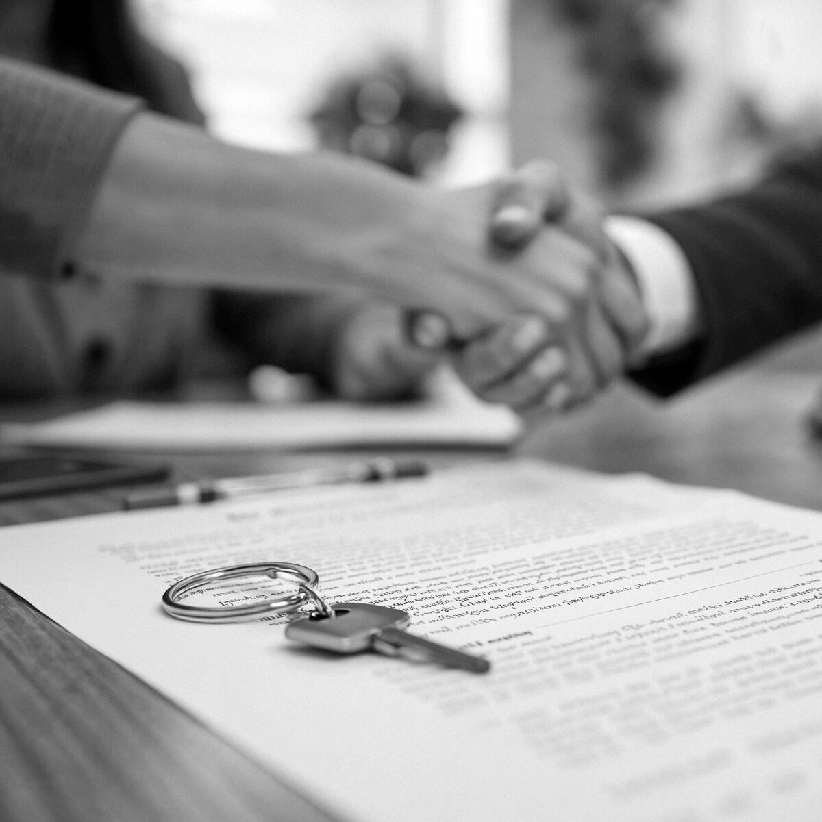 Két ember kezet fog egy asztalnál, az előtérben ingatlan adásvételi előszerződés, rajta egy lakáskulcs, amely az ingatlan adásvételi előszerződés kötésének folyamatát ábrázolja.