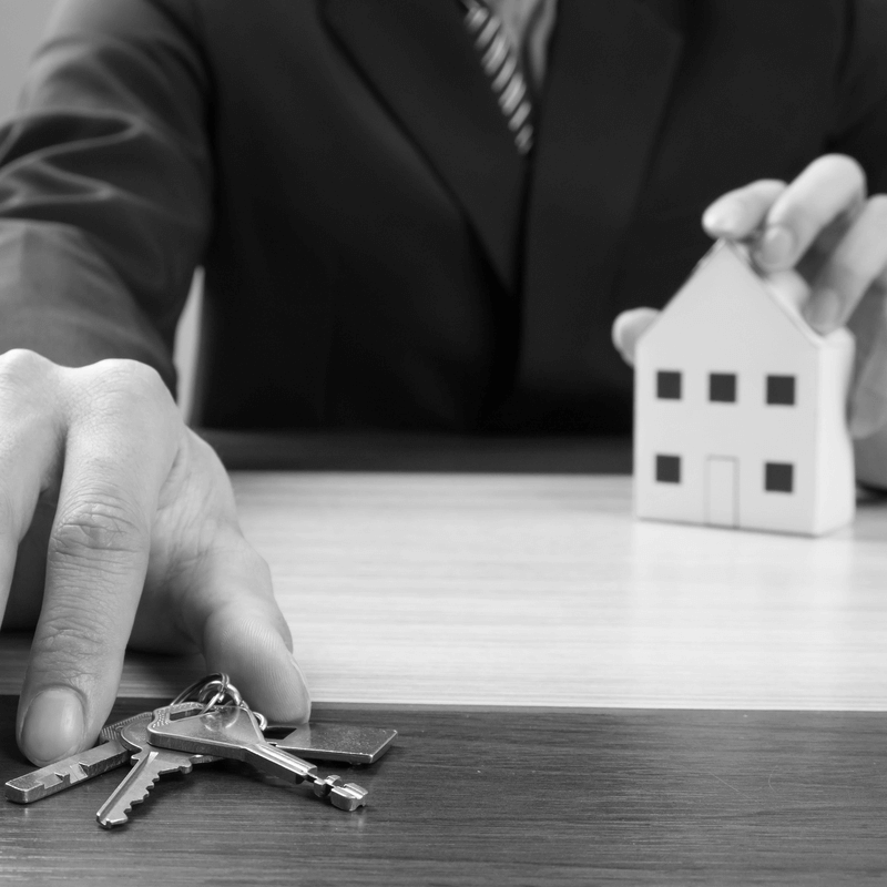 Üzletember ingatlan ajándékozás közben, egyik kezében házmakettel, másik kezében kulcsokkal – szimbolikus jelenet az ingatlan tulajdonjogának átadásáról.