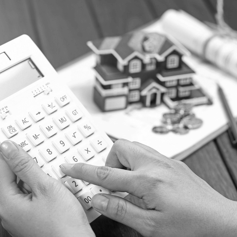 Ingatlan ajándékozás pénzügyi tervezése közben: kéz számológépen, háttérben házmodell és érmék – a vagyoni átadás adózási és számviteli szempontjai.