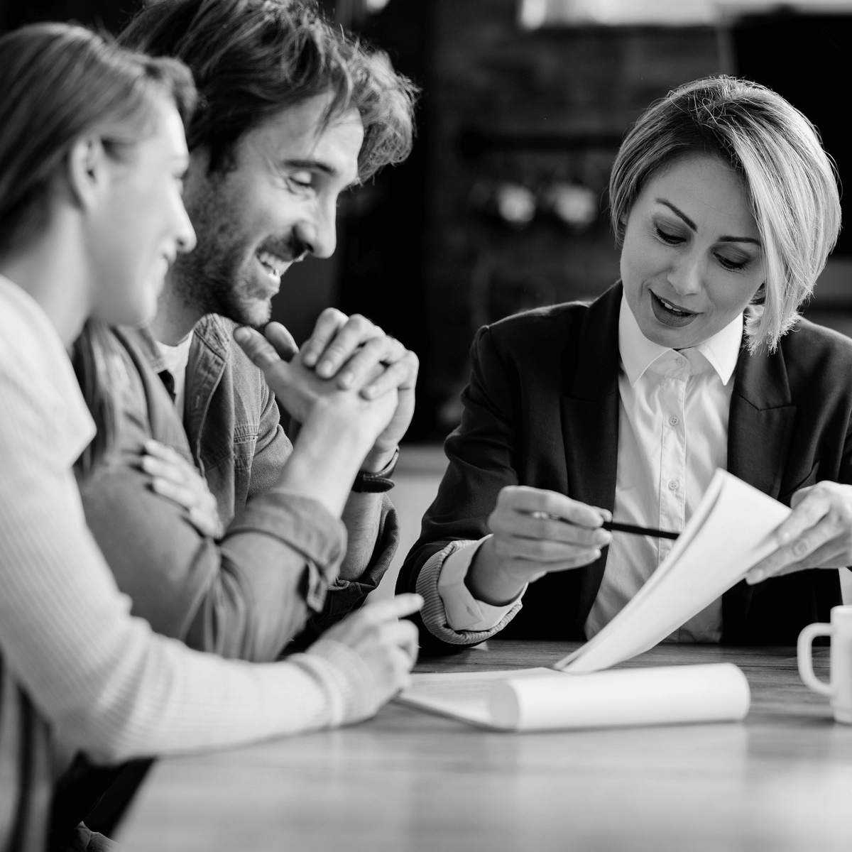 Fiatal pár egy ingatlanjogász segítségével tekinti át az ingatlan adásvételhez kapcsolódó szerződés részleteit egy otthonos környezetben, bizalmi légkörben zajló megbeszélés során.