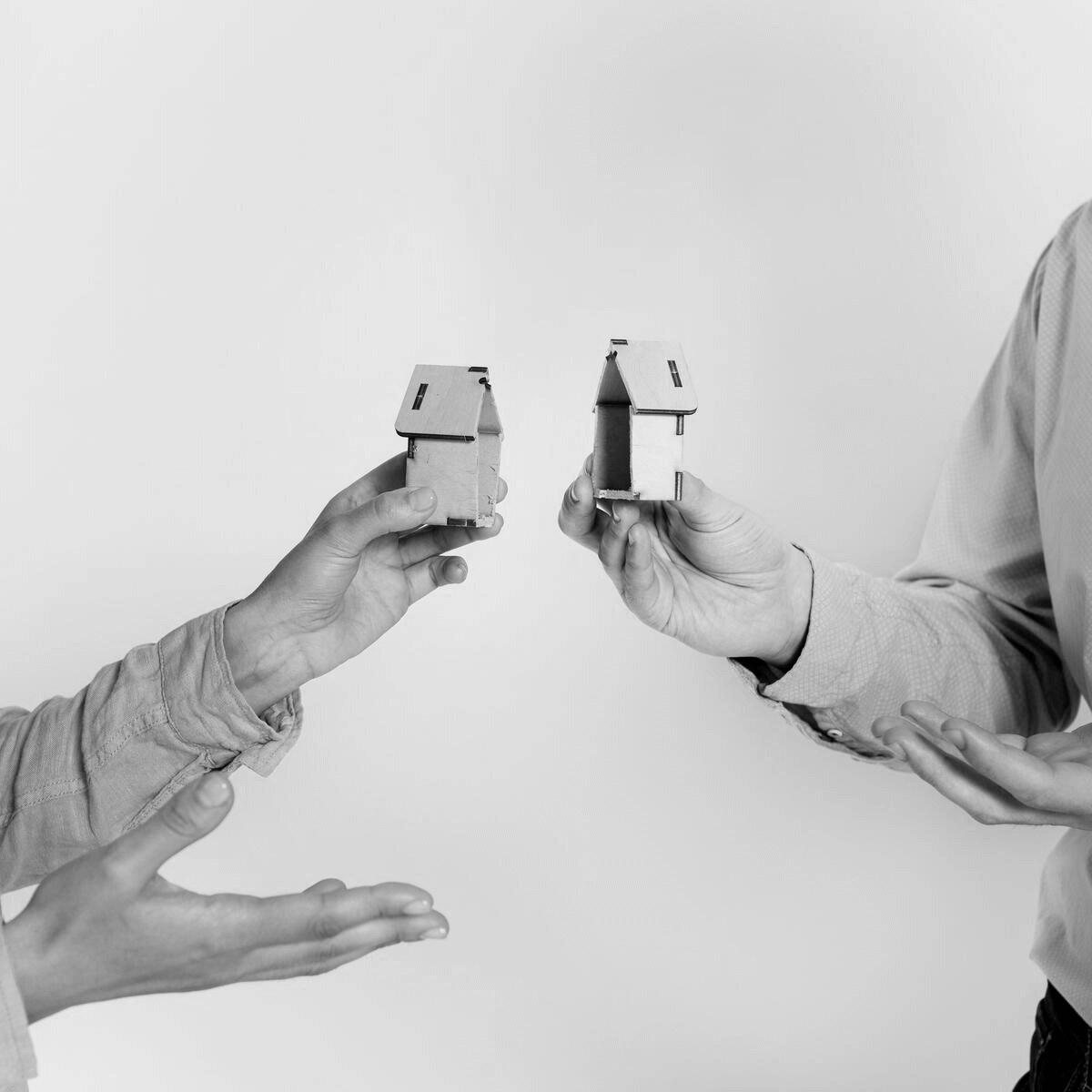 Két ember kezében kis házmakettek, amelyek egy ingatlan megosztását szimbolizálják, utalva a közös tulajdon megszüntetése jogi folyamatára.