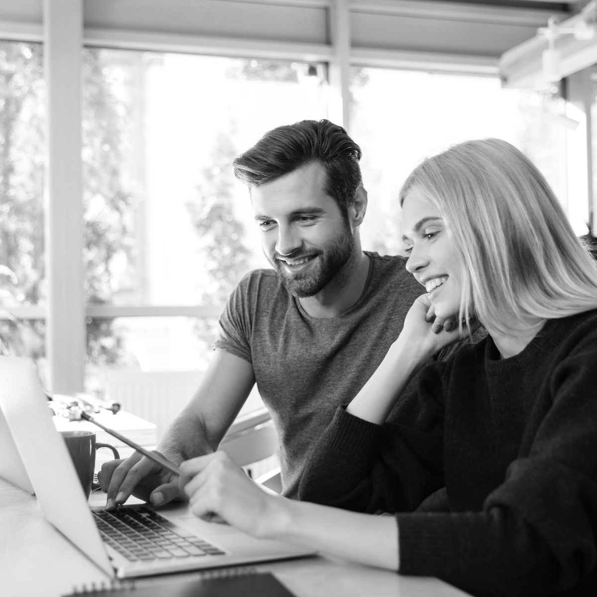 Mosolygó fiatal pár laptopon intézi online ingatlanügyeit egy világos, modern környezetben, miközben az ingyenes tulajdoni lap lekérése folyamatát végzik.